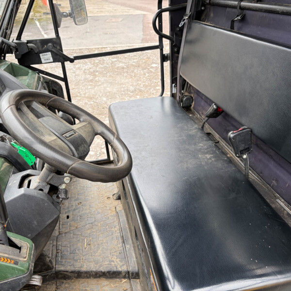 Interior view of a tractor cab: steering wheel, dusty dashboard controls, and a black vinyl seat beside a metal floor.