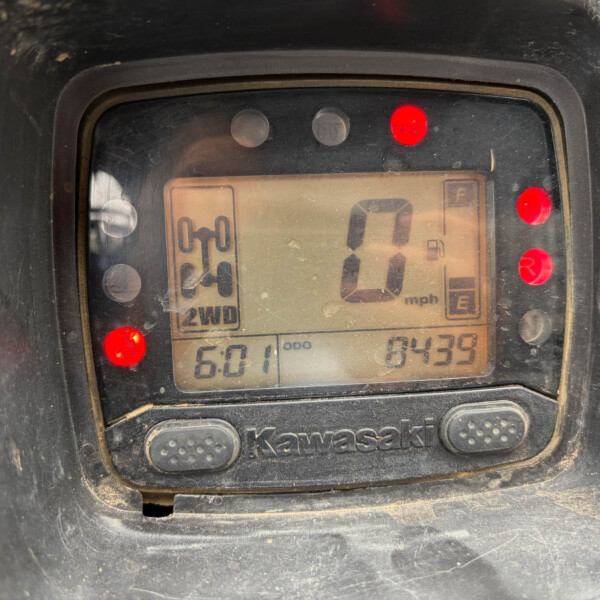 Kawasaki motorcycle digital gauge with speed readout at 0 mph, red warning lights on, and odometer reading visible; dusty surface around the display.