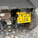 Rear view of an off-road vehicle showing a bright yellow license plate, exhaust pipe, and Mud-covered chassis and tire area.