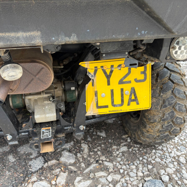 Rear view of an off-road vehicle showing a bright yellow license plate, exhaust pipe, and Mud-covered chassis and tire area.