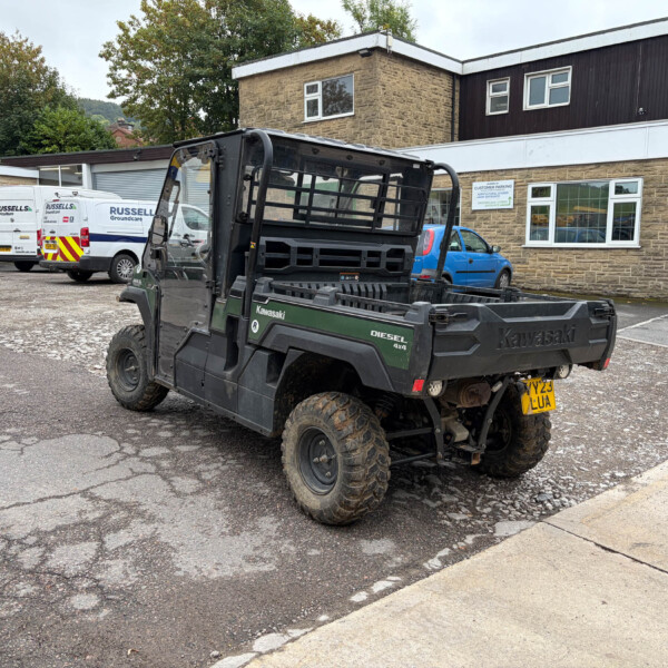 Black Kawasaki Diesel 4x4 utility vehicle in a parking lot, with white vans and a brick building in the background.