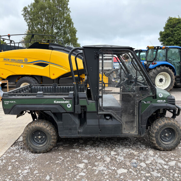 Bright yellow New Holland BigBaler 890 Plus baler parked in an outdoor equipment yard, with forklifts and a blue tractor nearby.