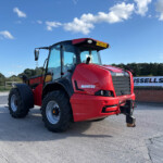 Red Manitou tractor viewed from the front-left, showing the cab, big tires, and license plate YW23 BVG against a clear blue sky.