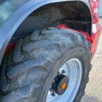 Close-up of a large tractor rear tire mounted on a red tractor, showing dirt and tread pattern with an orange side reflector visible near the rim.