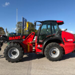 Red Manitou loader tractor with front attachment in a dealership lot under a clear blue sky.