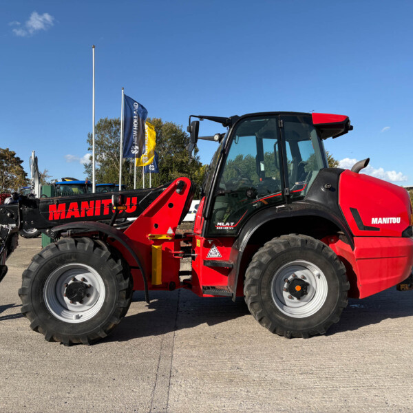 Red Manitou loader tractor with front attachment in a dealership lot under a clear blue sky.