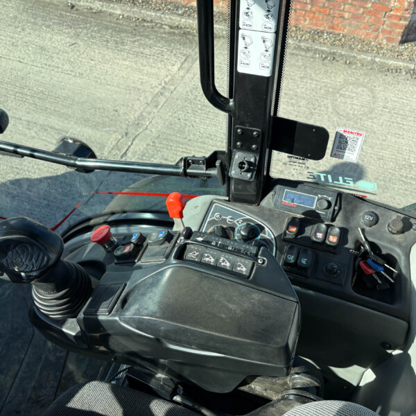 Interior view of a tractor cab showing a black joystick, row of control buttons, and an instrument panel near the driver's seat.