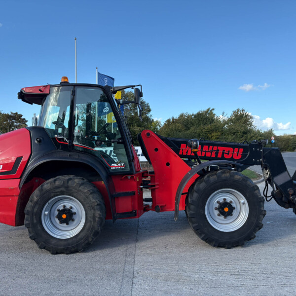 Red Manitou telehandler with large tires and lifted arm, parked on a paved lot under a blue sky.