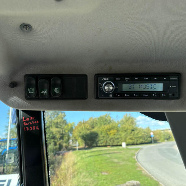 Dashboard controls and a radio unit mounted in a vehicle, with a construction yard visible through the windshield outside.