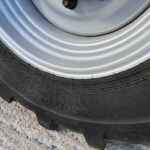 Close-up of a metal car wheel and black rubber tire on a rough concrete surface.