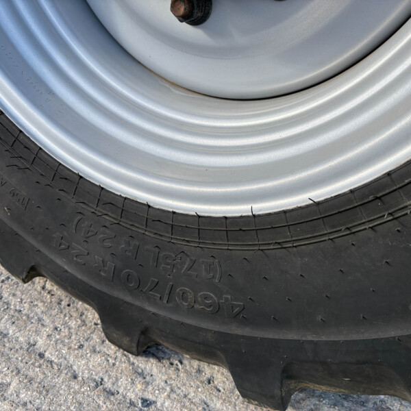 Close-up of a metal car wheel and black rubber tire on a rough concrete surface.