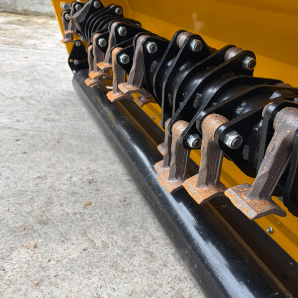 Close-up of rusted metal track links and bolts on a yellow construction machine frame.