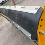 Close-up of a row of bolts securing a metal plate to a yellow industrial machine frame.