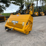 Row of yellow construction machines with lifting arms parked on a paved lot, trees in the background.