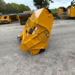 Yellow industrial machinery with large angled housing in a yard, multiple machines in background and trees beyond.