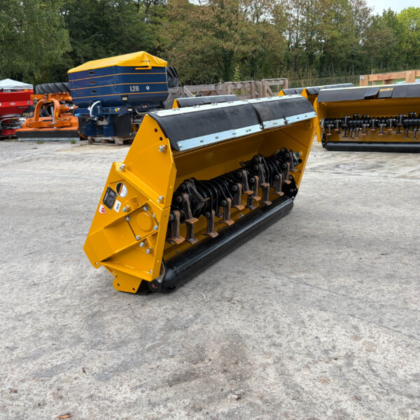 Yellow agricultural header with rotating blades and rollers, parked in an outdoor equipment yard with other machines in the background.