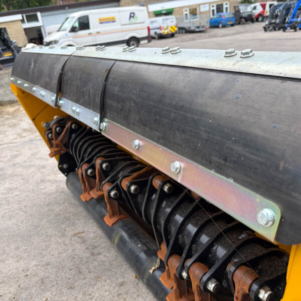 Close-up of a yellow construction machine’s roller system with metal guards and bolts; rusted gears visible beneath.