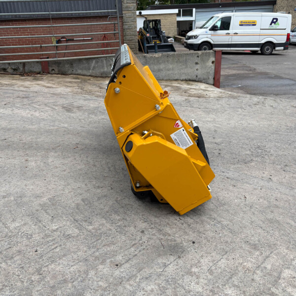 Close-up of a yellow industrial attachment on wheels in a gravel yard, with white vans in the background.