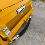 Close-up of a yellow industrial machine with warning stickers and a thick black hose on a rough concrete surface close to the device.