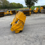Row of yellow industrial attachments lined up on a concrete yard with trees in the background, outdoor storage