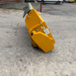 Yellow metal industrial equipment on wheels standing on a concrete parking lot with warning stickers and cars in the background.