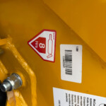 Red diamond hazard label on yellow equipment showing a bottle icon and '8 hrs' warning.
