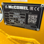 Close-up of a black metal identification plate on yellow industrial equipment, showing the MCCONNEL branding, serial and model numbers and a QR code.