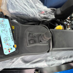 Close-up of a car's center console with a diagram sticker, red emergency button, and exposed wiring under plastic wrap.