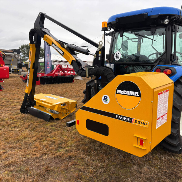 Blue tractor with yellow McConnel implement attached, on display at an outdoor farming equipment show