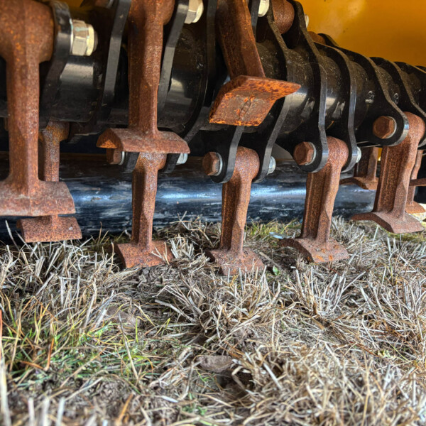 Close-up of rusty metal blades and supports from agricultural machinery resting on dry grass.