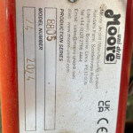 Close-up of a weathered metal nameplate on a red device, with boxes for model and serial numbers (text is largely unreadable).