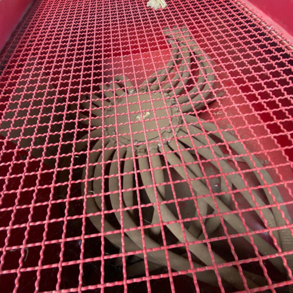 Red metal grid/mesh covers a large opening, with a tied rope at the top and visible inner curved metal components beneath.