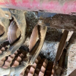 Dusty, cluttered attic showing wooden beams, rusted metal brackets, and dirt or debris scattered around.