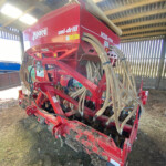 Red Moore uni-drill seed drill with numerous hoses attached, stored inside a wooden-shed barn.