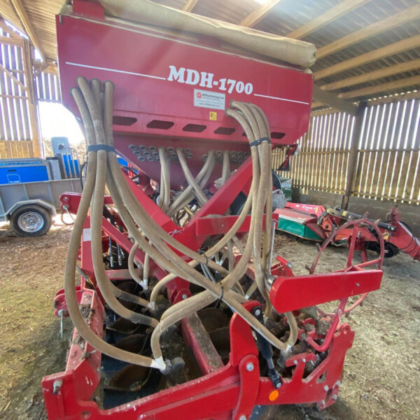 Red seed drill/planter with many beige hoses, stored in a wooden shed