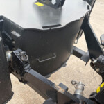 Close-up of a black industrial machine frame with hitch and hydraulic components, showing dirt and wear.