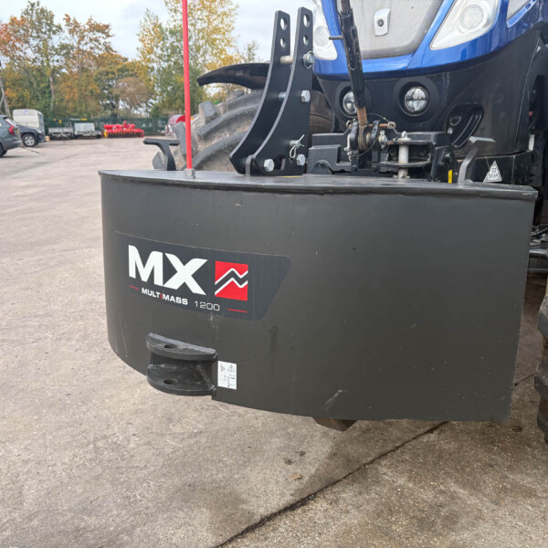 Close-up of a heavy tractor front attachment with 'MX Multimass 1200' branding in a yard with parked cars in the background