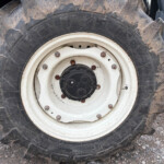 Close-up of a muddy tractor tire and white wheel hub with rusted bolts showing heavy tread and gravel ground nearby