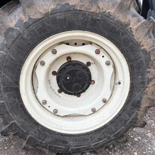 Close-up of a muddy tractor tire and white wheel hub with rusted bolts showing heavy tread and gravel ground nearby