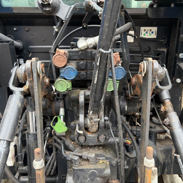 Close-up of a tractor's hydraulic valve block with blue, green, and orange caps and tangled hosesened fittings (informative)