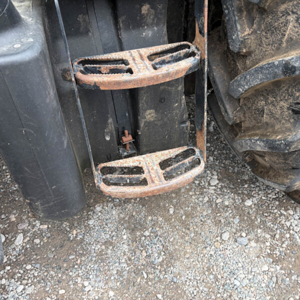 Close-up of a rusted metal step between tractor wheels on a dirt surface, showing heavy wear and grime.