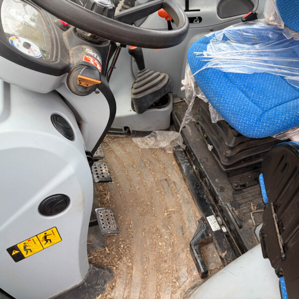 Interior of a dusty vehicle cab showing the steering wheel, pedals, and a blue fabric seat covered in plastic wrap.