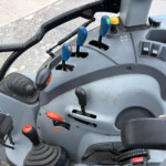 Close-up of a tractor cab interior showing multiple color-coded levers (blue and orange) and pedals near a gray dashboard.