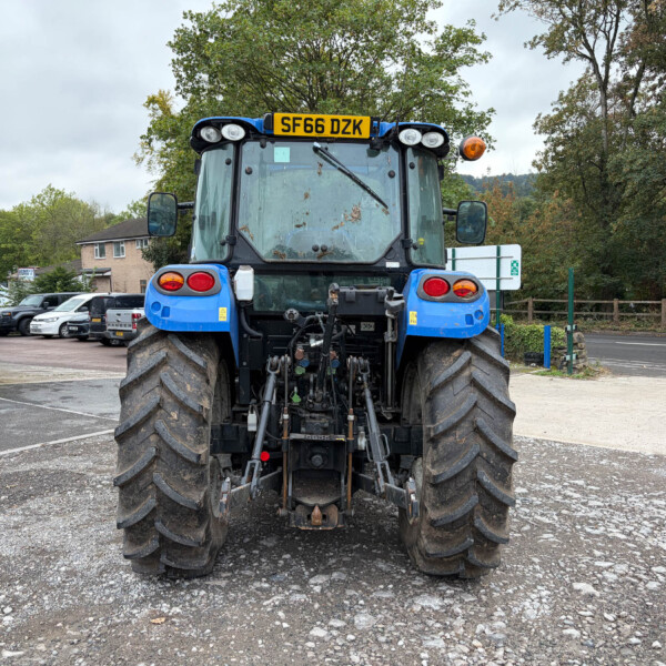 Rear view of a blue tractor with large muddy tires parked in a lot, license plate SF66 DZK visible on top.