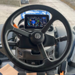 Interior view of a vehicle cabin with a large steering wheel and digital instrument cluster displaying RPM and gear information.