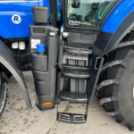Close-up of a blue semi-truck cab with black steps, ladder, and a large front tire nearby.