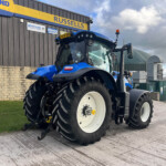 Large blue tractor with oversized tires parked outside a building with a yellow Russell’s sign and a white van in the background.