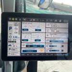 Tablet mounted in a tractor cab displaying a multi-panel system monitor with engine hours, speed, hydraulics, and other controls