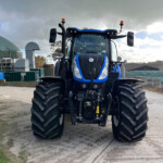 Front view of a blue tractor with oversized tires and orange warning lights in an industrial yard.