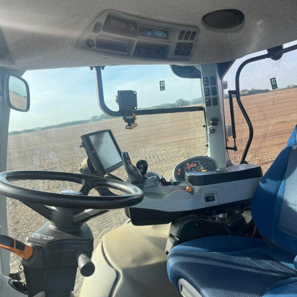 Interior view of a tractor cabin showing the steering wheel, blue cushioned seat, and dashboard controls near the windshield.